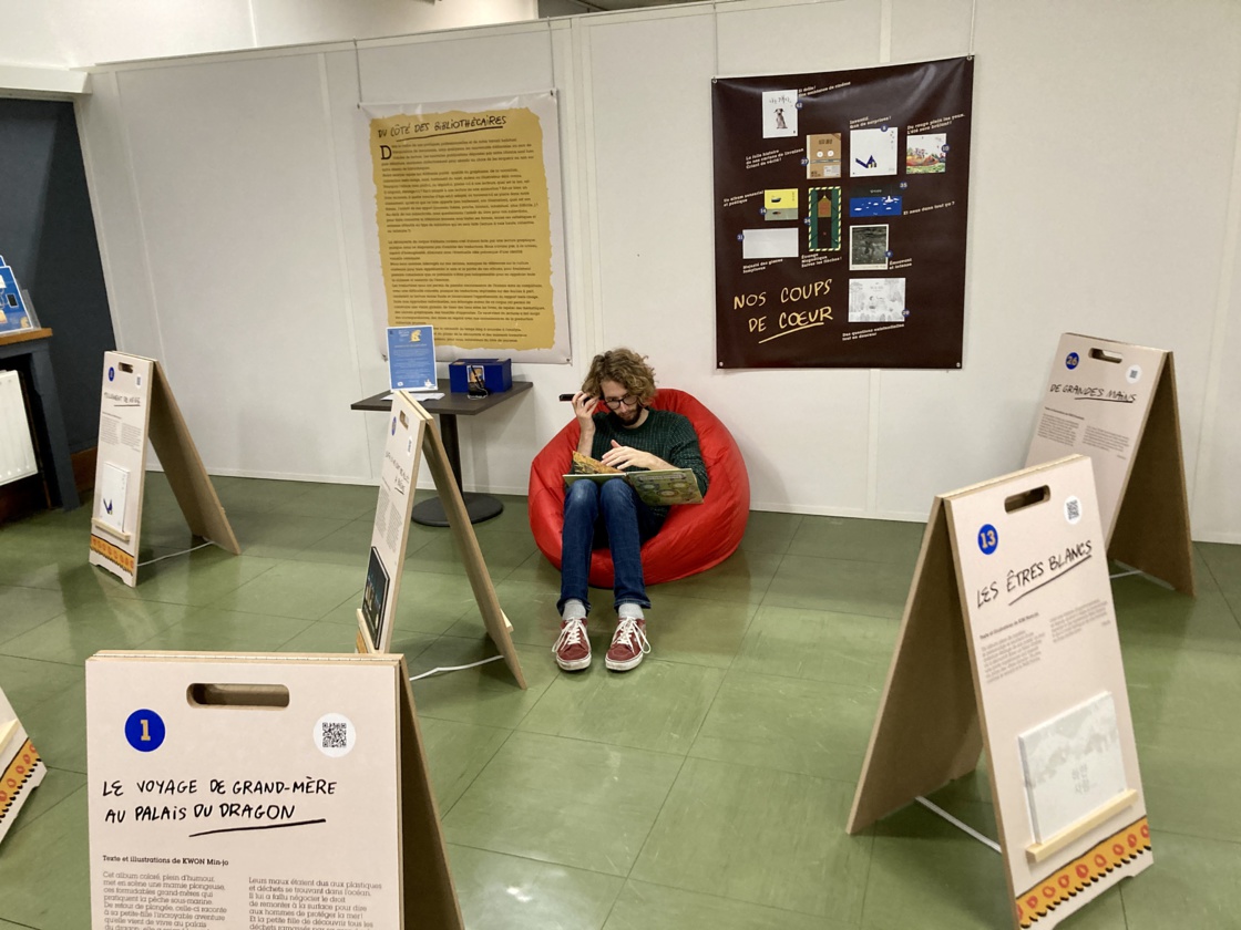 Ce jeune homme écoute sur son téléphone l’enregistrement de la version française, accessible via les codes QR de chacun des panneaux. Ce jeune homme écoute sur son téléphone l’enregistrement de la version française, accessible via les codes QR de chacun des panneaux.